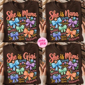 K&ouml;nnte beinhalten: Vier braune Rundhals-T-Shirts mit den Aufschriften "She is Mama", "She is Nana", "She is Gigi" und "She is Mimi" in rosa Schrift. Jedes Shirt hat ein farbenfrohes Schleifendesign mit W&ouml;rtern wie "Strong", "Beautiful" und "Victorious".