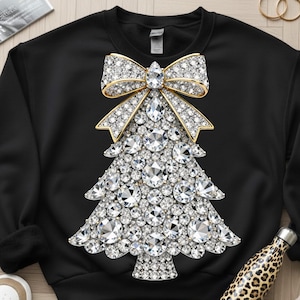 May include: Black sweatshirt featuring a sparkling Christmas tree design. The tree is adorned with numerous clear, glittering crystals and topped with a gold bow. A festive and eye-catching holiday-themed garment.