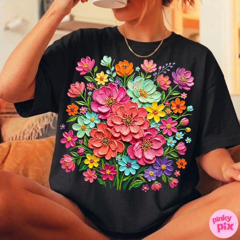 May include: Black t-shirt featuring a vibrant floral design. The design showcases a bouquet of colorful flowers in shades of pink, orange, yellow, blue, and purple. The flowers appear to have a textured, three-dimensional effect.