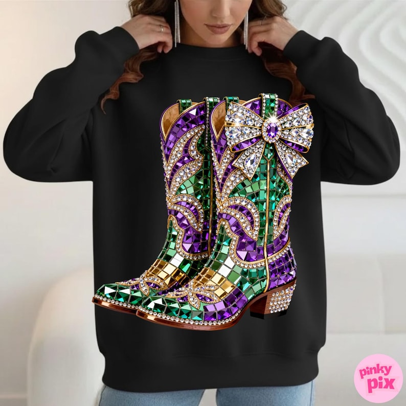 May include: Black sweatshirt featuring a vibrant graphic of jeweled cowboy boots. The boots are adorned with green, purple, and gold mosaic-style embellishments, and a large crystal bow. The boots have a brown heel.