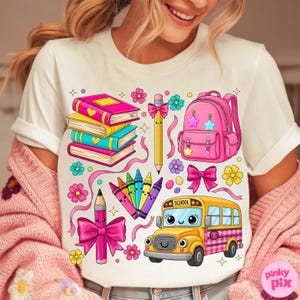 Pu&ograve; includere: T-shirt bianca con grafica a tema scolastico. Il design include una pila di libri, uno zaino rosa, un autobus scolastico giallo, matite, pastelli e fiori. La maglietta ha girocollo e maniche corte.