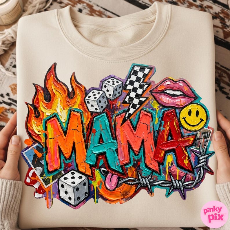 May include: Cream-colored sweatshirt with a vibrant graffiti-style design. The word "MAMA" is prominently displayed in bold, colorful letters, surrounded by flames, dice, a lightning bolt, lips, a smiley face, and barbed wire.