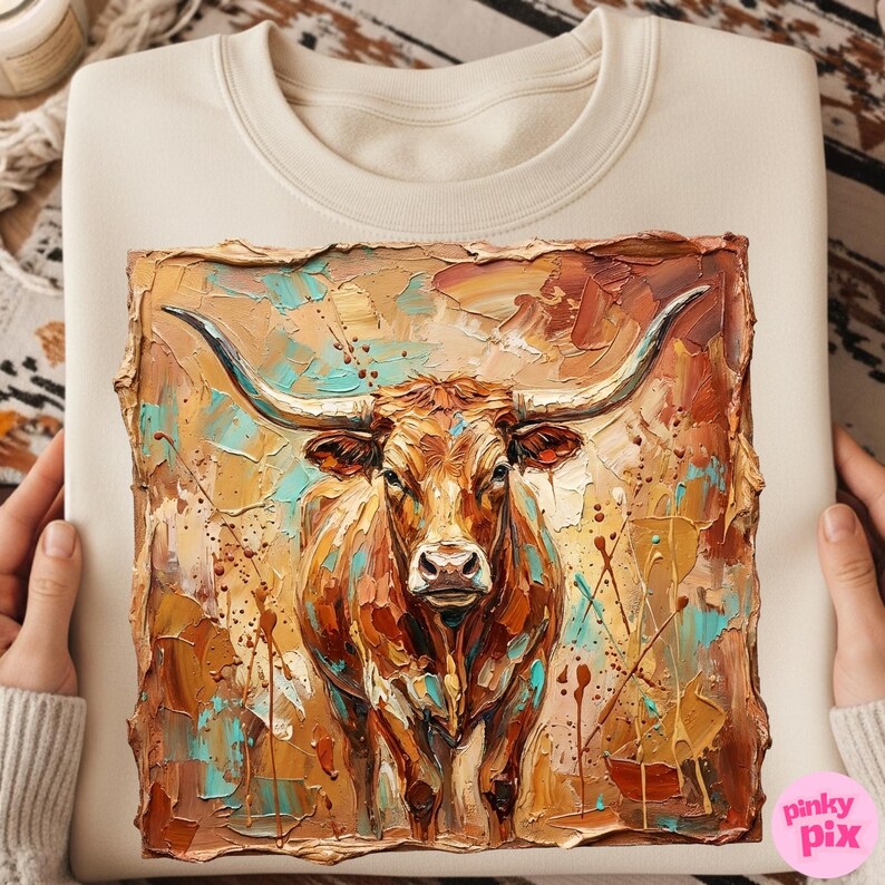May include: Cream-colored sweatshirt featuring a textured, colorful painting of a longhorn bull. The artwork uses shades of brown, orange, and teal, with visible brushstrokes. The bull faces forward, showcasing its large horns.