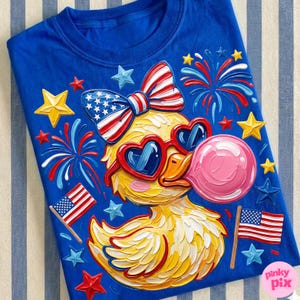 May include: Blue t-shirt featuring a yellow duck wearing heart-shaped sunglasses and a bow, both in red, white, and blue. The duck is blowing a pink bubble and surrounded by fireworks, stars, and American flags.