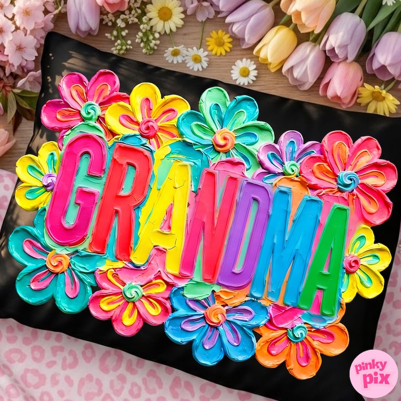 May include: Black pillow with a vibrant floral design and the word "GRANDMA" in colorful, raised lettering. The flowers are in shades of pink, yellow, blue, and orange, creating a cheerful and eye-catching aesthetic.