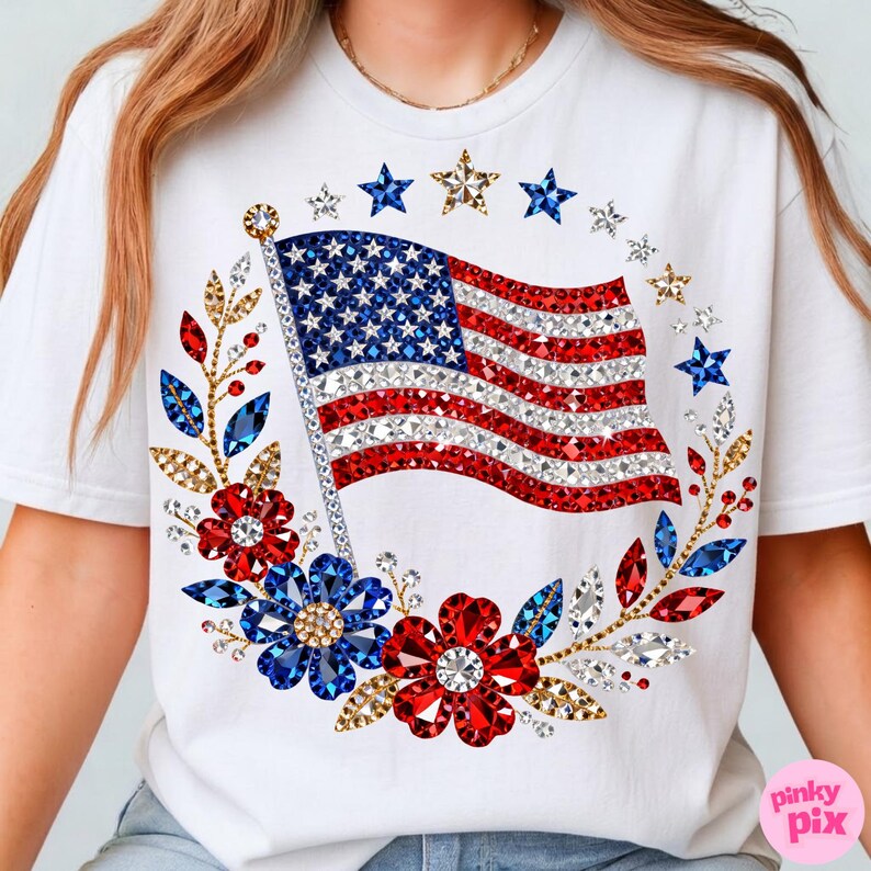 May include: White t-shirt featuring a sparkling American flag design with red, white, and blue embellishments. The flag is surrounded by a floral wreath with stars, leaves, and flowers. The shirt has a crew neck.