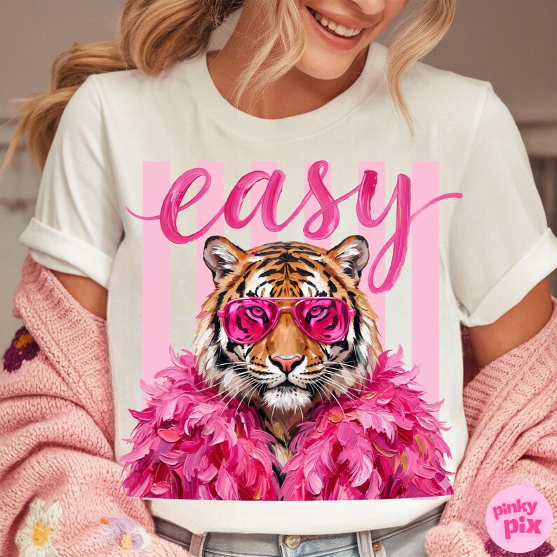 May include: White t-shirt featuring a tiger wearing pink sunglasses and a pink feather boa. The word "easy" is written in pink script above the tiger, with pink vertical stripes in the background.