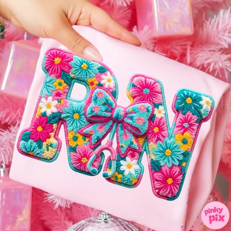 May include: A light pink pillow with the embroidered letters "RN" in a floral design. The letters are filled with pink, turquoise, yellow, and white flowers. A turquoise bow and stethoscope are between the letters.