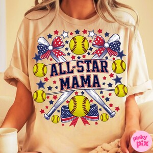 May include: Beige t-shirt with a softball-themed design. The design includes yellow softballs, baseball bats, red and blue bows, and stars. The text "ALL-STAR MAMA" is prominently displayed in navy blue and white.