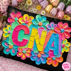 Op de afbeelding: Zwart kussen met kleurrijke, getextureerde bloemen en de letters "CNA" in heldere kleuren. De bloemen zijn in tinten roze, geel, blauw en oranje. Het kussen is omringd door bloemen.