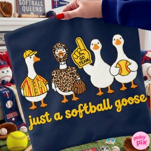 May include: Navy blue pillowcase with a whimsical design of four cartoon geese dressed in softball gear. The text "just a softball goose" is in yellow script. One goose wears a jersey, another a leopard print outfit.