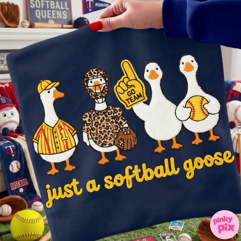 May include: Navy blue pillowcase with a whimsical design of four cartoon geese dressed in softball gear. The text "just a softball goose" is in yellow script. One goose wears a jersey, another a leopard print outfit.
