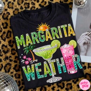 Peut inclure: T-shirt noir avec l'inscription "MARGARITA WEATHER" en lettres orn&eacute;es de bijoux. Le motif comprend un verre &agrave; margarita, un cocktail rose, un soleil, un palmier et des tranches de citron vert. Le t-shirt a un col rond.