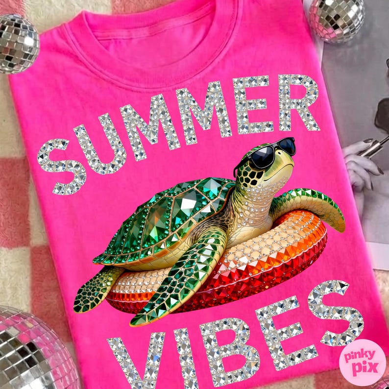 May include: Hot pink t-shirt with the words "SUMMER VIBES" in rhinestone lettering. A bejeweled green sea turtle wearing sunglasses is on a red and orange float. The shirt has a crew neck.