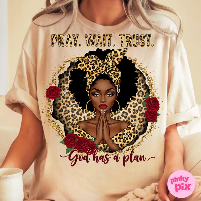 May include: A beige t-shirt with a black and brown leopard print design featuring a woman with a leopard print headband and a gold glitter background. The text "Pray. Wait. Trust. God has a plan." is printed on the shirt.