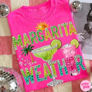 Peut inclure: Un t-shirt rose vif avec l'inscription "MARGARITA WEATHER" en strass verts, jaunes et bleus &eacute;tincelants. Le motif comprend un verre &agrave; margarita, un cocktail rose, un palmier et un soleil.