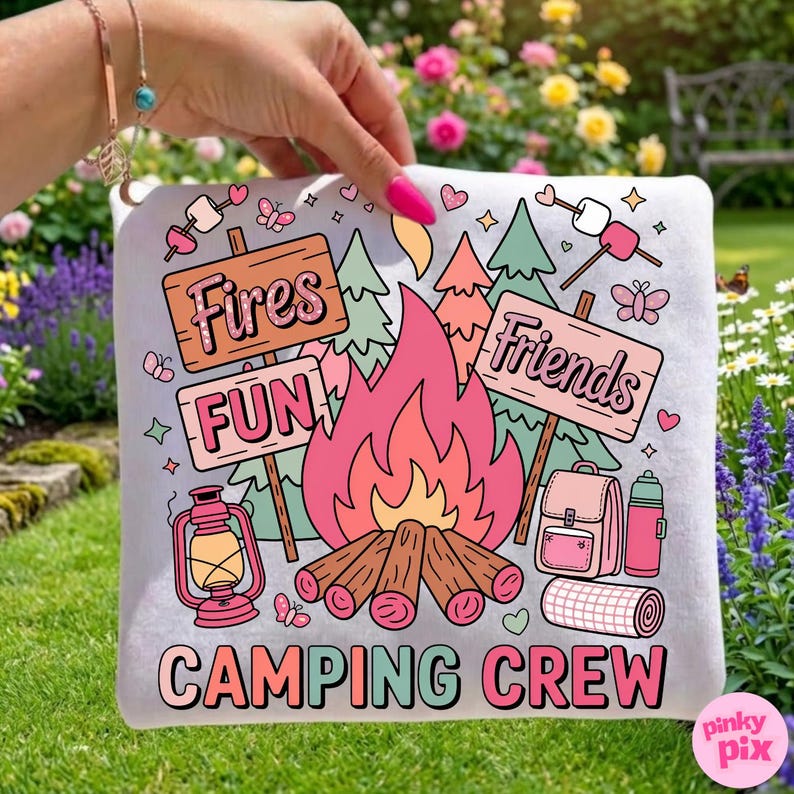 May include: A white camping-themed pillow with a colorful design. The design includes a campfire, signs that say "Fires", "Fun", and "Friends", and the words "Camping Crew". Other elements include a lantern, backpack, and marshmallows.