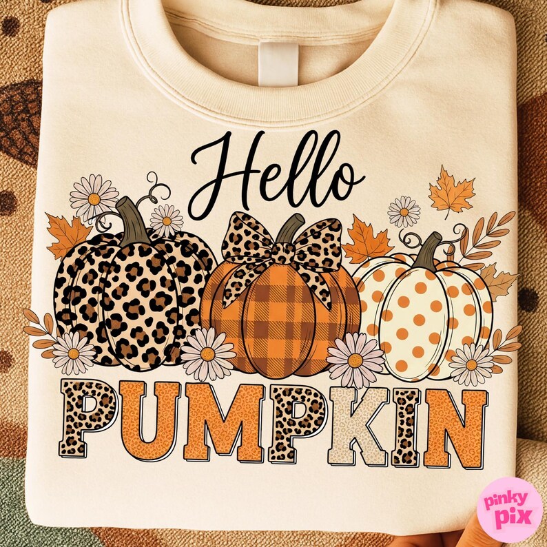 Op de afbeelding: Cr&egrave;mekleurige sweatshirt met de tekst "Hello Pumpkin" en drie ge&iuml;llustreerde pompoenen. De pompoenen hebben verschillende patronen, waaronder luipaardprint, ruitjes en stippen. Bloemen- en bladaccenten omringen de pompoenen.