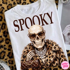 May include: A white t-shirt featuring the brown text SPOOKY above a graphic of a skull wearing leopard print sunglasses, a faux fur leopard print coat, a large crystal statement necklace, and holding a brown quilted handbag with a gold chain.