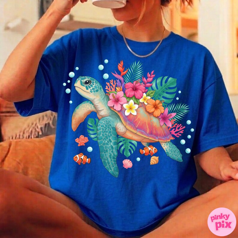 May include: Royal blue t-shirt featuring a colorful illustration of a sea turtle with a floral design. The turtle has a teal shell and is surrounded by tropical flowers, coral, and fish. The shirt has short sleeves.