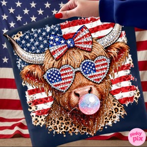 May include: A navy blue pillow featuring a Highland cow with patriotic sunglasses and a bow, both adorned with the American flag. The cow is blowing a bubble and has a leopard print pattern. The background includes an American flag.
