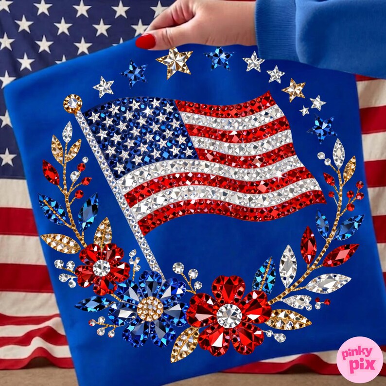 May include: A royal blue garment featuring a sparkling American flag design. The flag is embellished with red, white, and blue rhinestones. The design includes a floral wreath with red and blue flowers and gold accents. The background shows an American flag.