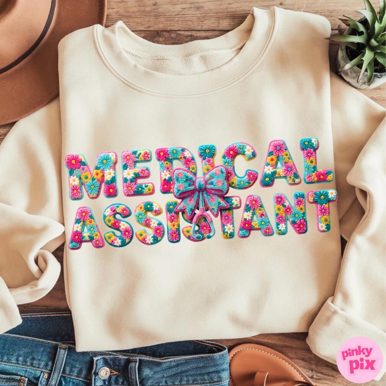 May include: Cream-colored sweatshirt with the words "MEDICAL ASSISTANT" in colorful floral letters. A blue bow is centered above the word "ASSISTANT". The sweatshirt is made of a soft material.