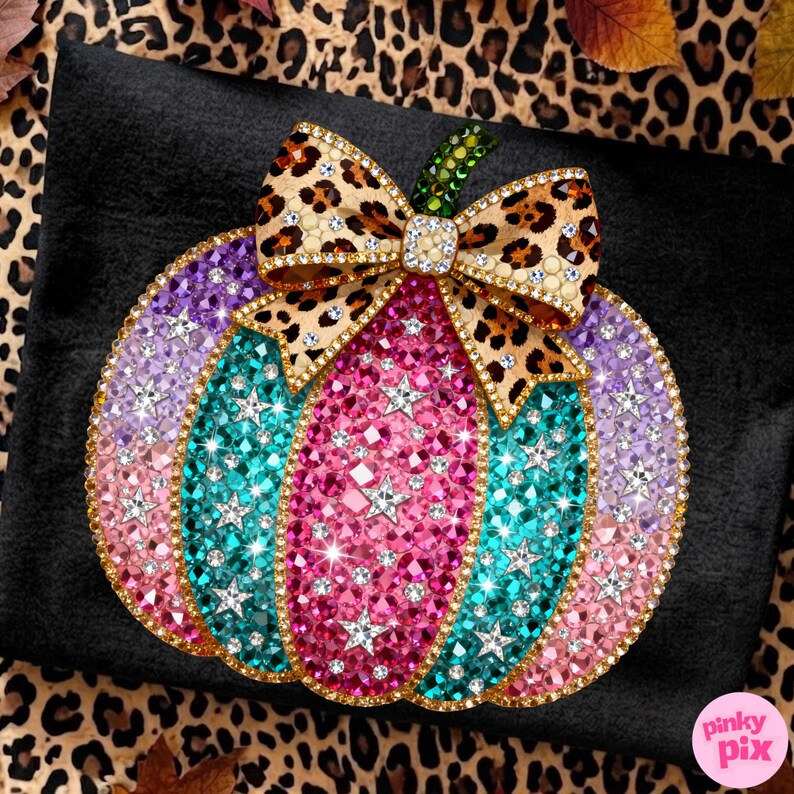 Op de afbeelding: Een pompoenvormige decoratie bedekt met veelkleurige strass-steentjes, met verticale segmenten in roze, talingblauw en lavendel. Een strik met luipaardprint en heldere kristallen zit aan de bovenkant, geaccentueerd door een groene steel. De tekst Pinky Pix is zichtbaar.