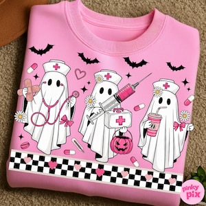 May include: Pink sweatshirt featuring a graphic of three ghost nurses with medical tools and a jack-o'-lantern. The design includes bats, pills, and a checkered border with hearts. The text "pinky pix" is in the bottom right corner.