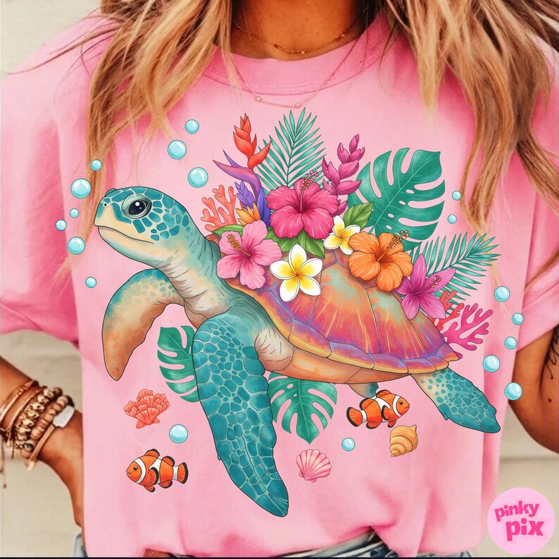 May include: Pink t-shirt featuring a colorful sea turtle design. The turtle has a blue shell and flippers, with a vibrant floral arrangement on its back. Tropical flowers, coral, and fish are also depicted.