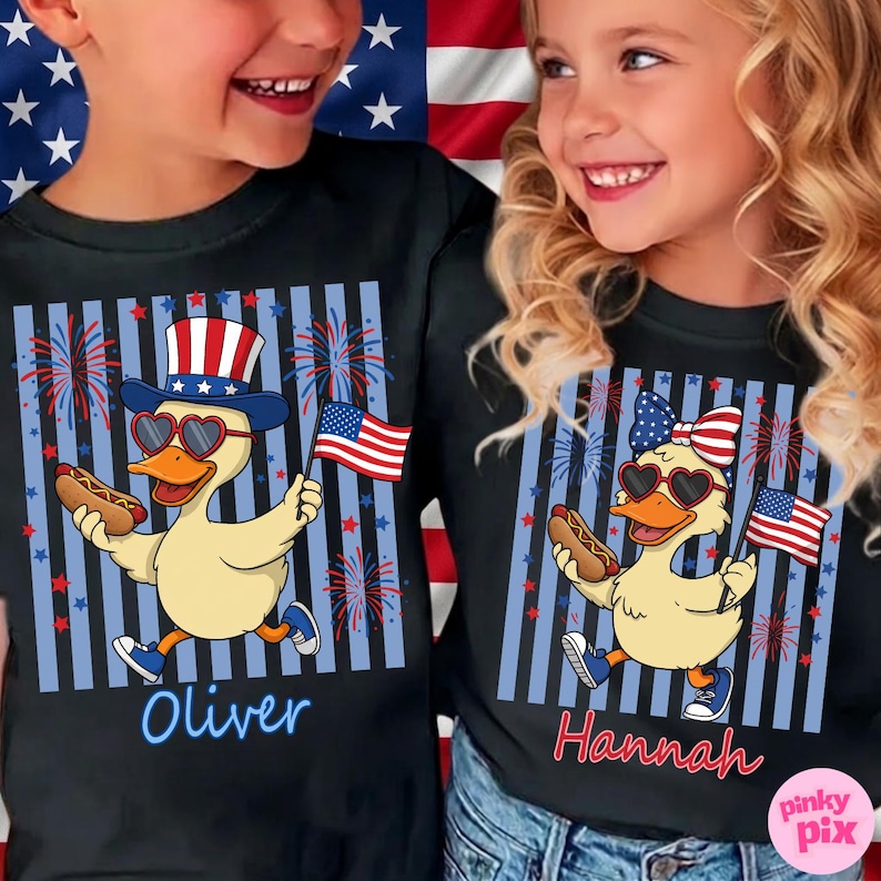 May include: Black t-shirts with a patriotic duck graphic. The duck wears heart-shaped sunglasses and a hat or bow with an American flag design, holding a hot dog and a flag. Names "Oliver" and "Hannah" are printed on the shirts.