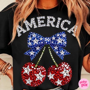 May include: Black t-shirt with the word "AMERICA" in silver glitter letters. A blue bow with white star accents sits above two red cherries with white star accents. The cherries have green stems.