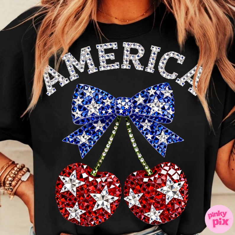May include: Black t-shirt with the word "AMERICA" in silver glitter letters. A blue bow with white star accents sits above two red cherries with white star accents. The cherries have green stems.