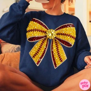 May include: Navy blue sweatshirt with a large, decorative bow. The bow is embellished with yellow and red rhinestones, and a central jewel. The sweatshirt is a solid color, and the bow is the main design element.