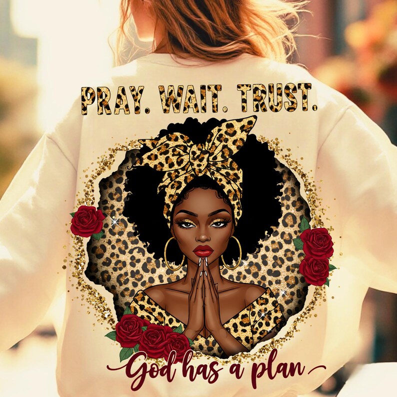 Pu&ograve; includere: Felpa color crema con grafica di una donna con foulard e abiti leopardati, circondata da rose rosse e glitter dorati. Il testo "PRAY. WAIT. TRUST." &egrave; in alto e "God has a plan" in basso.