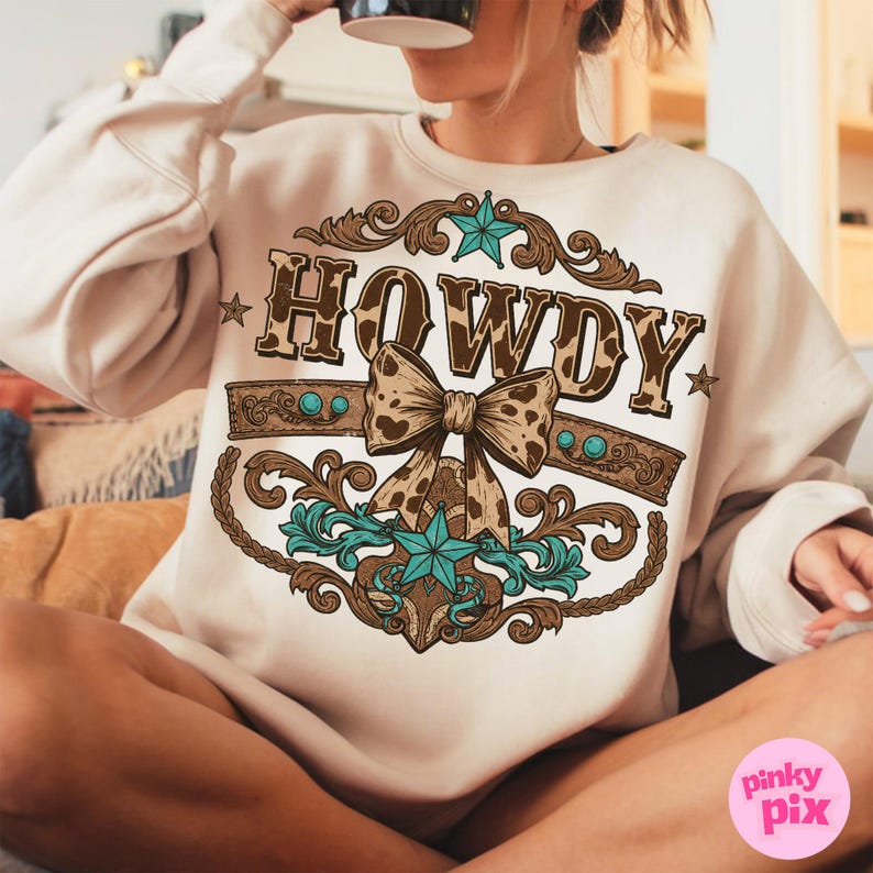Pu&ograve; includere: Una felpa color crema con un designo marrone e turchese che presenta la parola "HOWDY" con un fiocco marrone e bianco a pois.