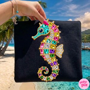 May include: Black clutch featuring a colorful, jeweled seahorse design. The seahorse is adorned with various colored gems, including turquoise, pink, yellow, and purple. The background shows a tropical beach scene.
