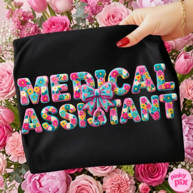 May include: Black t-shirt with the words "MEDICAL ASSISTANT" in colorful floral letters. A blue and pink bow and stethoscope graphic is centered between the words. The shirt is held up by a hand with red nail polish, surrounded by pink flowers.