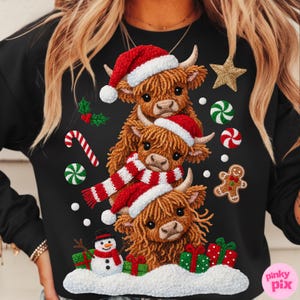 May include: Black sweatshirt featuring a festive design of three Highland cows wearing Santa hats and a red and white scarf. The design includes a snowman, gifts, and Christmas ornaments. A gold star and gingerbread man are also included.