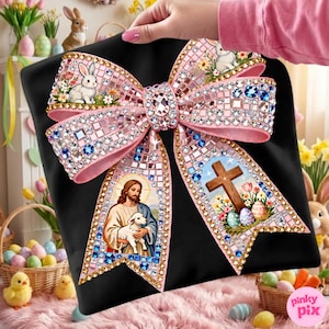 以下が含まれることがあります： モザイク模様の大きな装飾用ピンクのリボン。ウサギ、子羊を抱くイエス、イースターエッグの十字架の画像が特徴です。リボンはラインストーンで装飾され、黒い背景に配置されています。