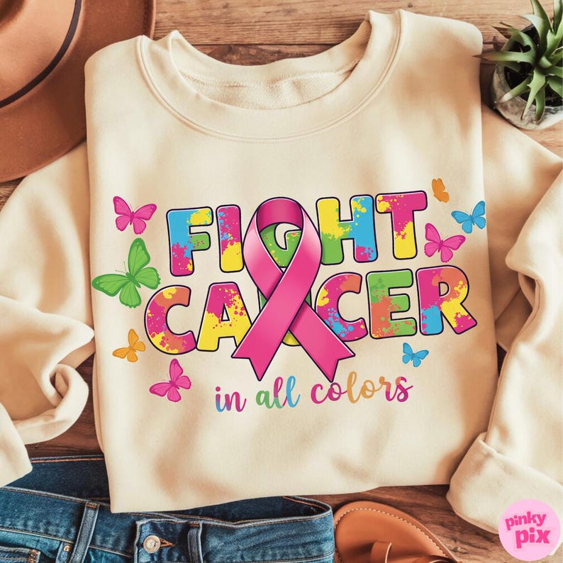 May include: Cream-colored sweatshirt with the words "FIGHT CANCER" in colorful, splattered letters, a pink ribbon, and butterflies. The phrase "in all colors" is below the main text.