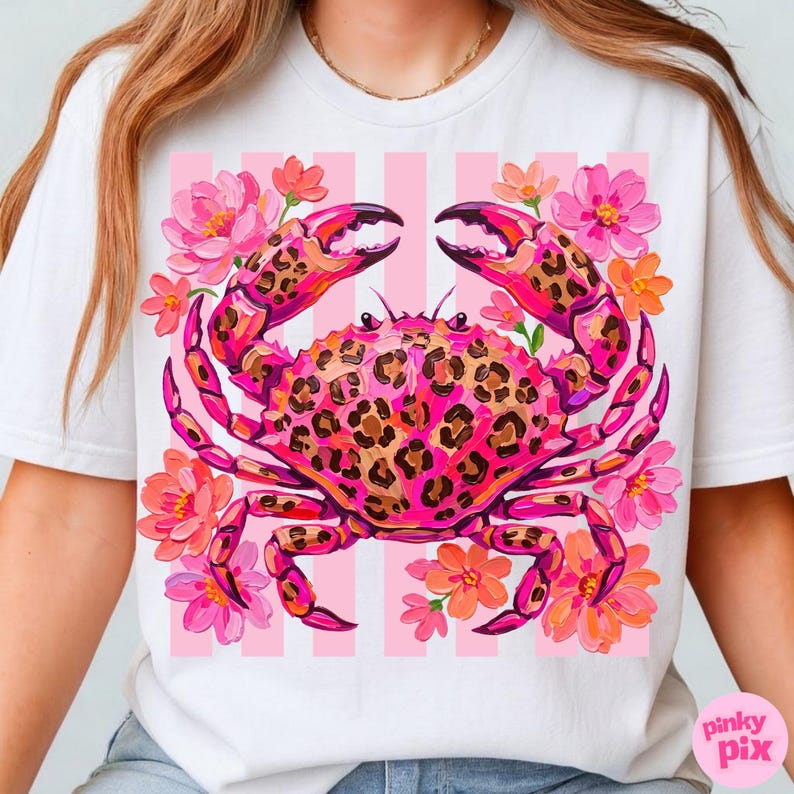 May include: White t-shirt featuring a vibrant pink crab with a leopard print design. The crab is surrounded by pink and orange flowers against a backdrop of pink and white stripes. The text "pinky pix" is in the bottom right corner.