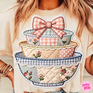 Puede incluir: Una camiseta color crema con un diseño apilado de tres cuencos decorativos con un lazo en la parte superior. Los cuencos tienen un diseño de patchwork con estampados florales y de cuadros vichy en colores pastel. El diseño está delineado con un borde blanco.