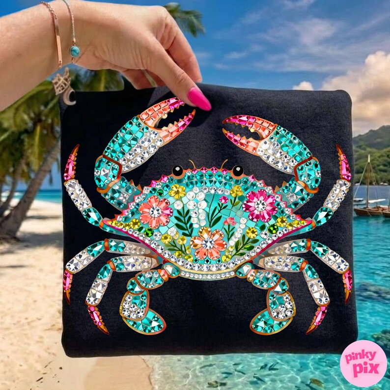 May include: Black square bag featuring a detailed crab design. The crab is adorned with turquoise, pink, and clear crystal-like embellishments, with floral accents. The bag is held against a beach backdrop, with the Pinky Pix logo in the corner.