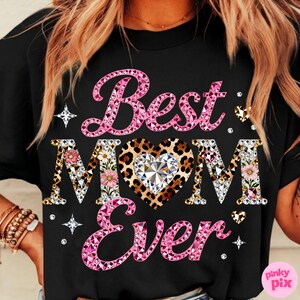 May include: Black t-shirt with the text "Best Mom Ever" in pink, leopard print, and floral designs. The word "Mom" features a heart-shaped leopard print with a diamond center. Rhinestones and star accents surround the text.