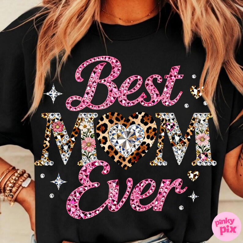 May include: Black t-shirt with the text "Best Mom Ever" in pink, leopard print, and floral designs. The word "Mom" features a heart-shaped leopard print with a diamond center. Rhinestones and star accents surround the text.