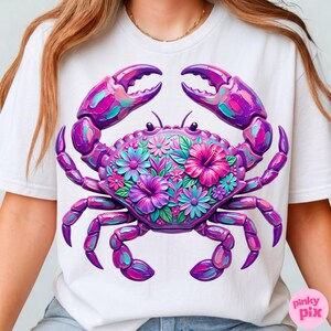 May include: White t-shirt featuring a vibrant, detailed crab design. The crab is rendered in shades of purple, pink, and teal, with floral accents on its shell. The design is centered on the shirt, creating a bold and eye-catching graphic.