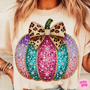 Op de afbeelding: Een cr&egrave;mekleurig t-shirt met een grote afbeelding van een pompoen versierd met roze, turquoise en paarse strass-steentjes, geaccentueerd door zilveren stervormige studs en een strik met luipaardprint met een groene strass-steel.