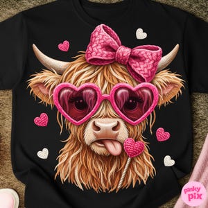 May include: Black t-shirt featuring a whimsical illustration of a Highland cow. The cow wears pink heart-shaped sunglasses and a matching bow. A heart-shaped lollipop and scattered hearts complete the design. The cow has long, shaggy brown fur.