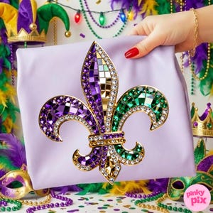 May include: A lavender-colored gift bag featuring a jeweled fleur-de-lis design in purple, green, and gold. The fleur-de-lis is embellished with rhinestones and mosaic-style accents. The bag is held by a hand with red nail polish, suggesting a festive theme.